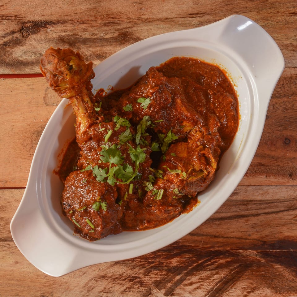 Swagat Indian Cuisine's chicken curry, garnished with fresh cilantro, served in a white dish on wood.